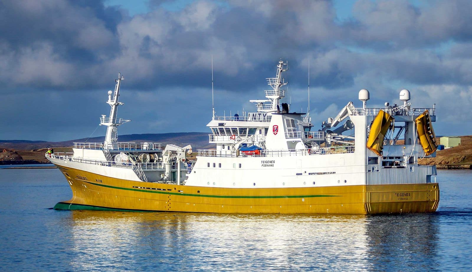 A yellow and white fishing vessel under way